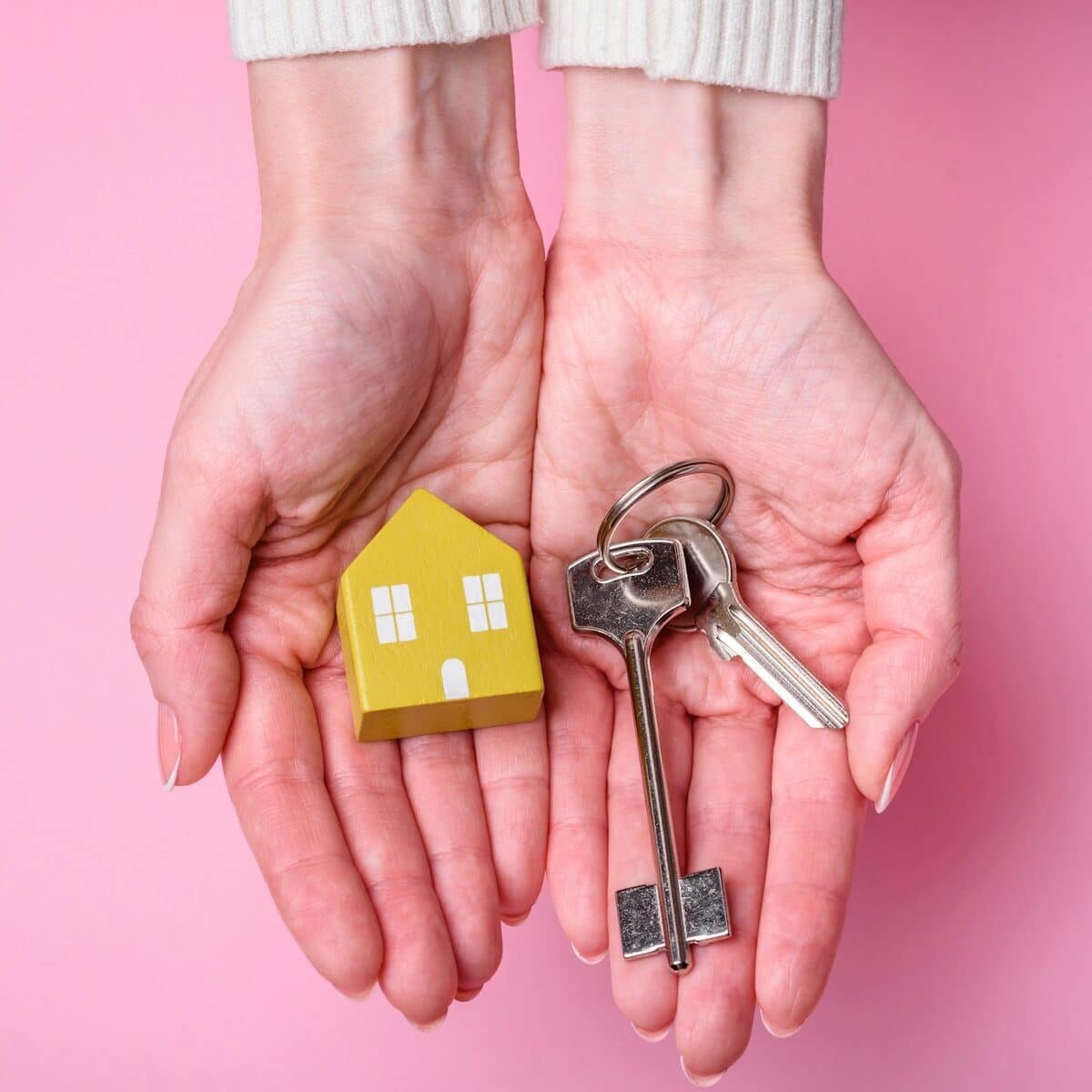 Female hands, a small wooden house and keys as an idea for investing in your own home